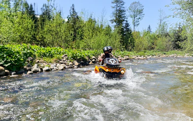 Visitors riding a quad bike through a river in Zakopane, surrounded by lush greenery.
