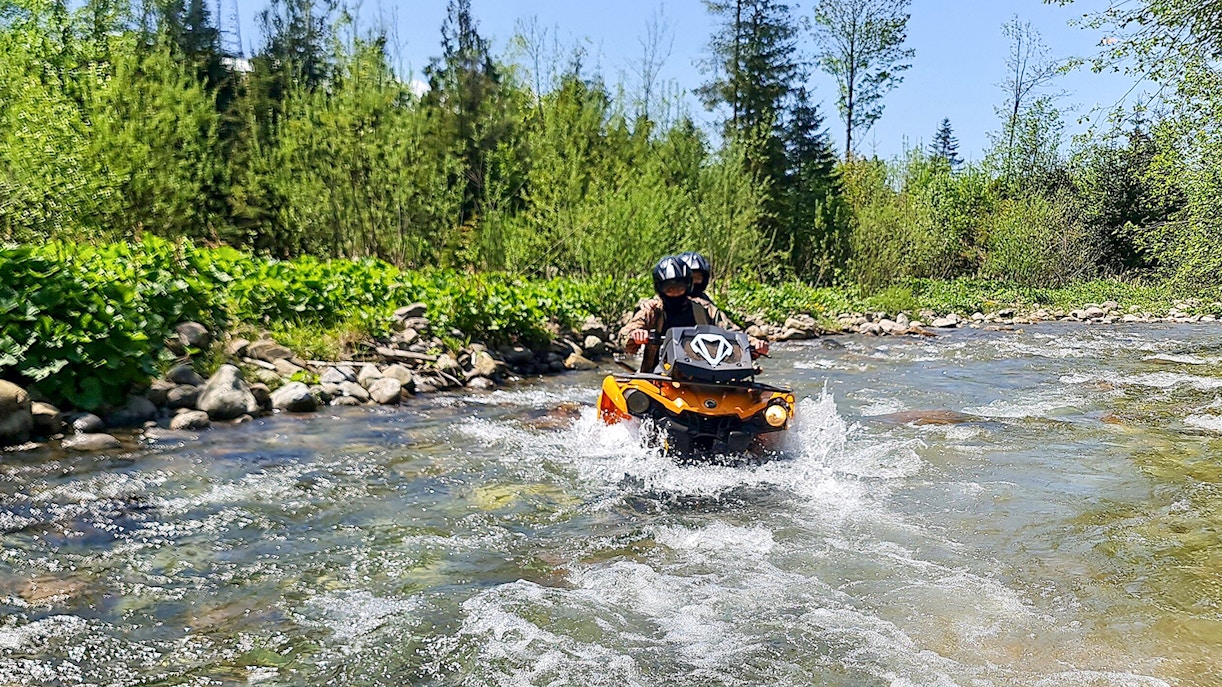 Visitors riding a quad bike through a river in Zakopane, surrounded by lush greenery.