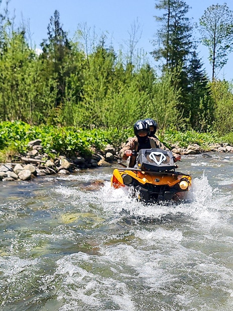 Visitors riding a quad bike through a river in Zakopane, surrounded by lush greenery.