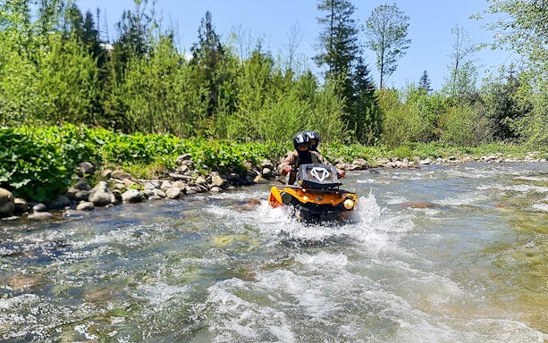 Visitors riding a quad bike through a river in Zakopane, surrounded by lush greenery.
