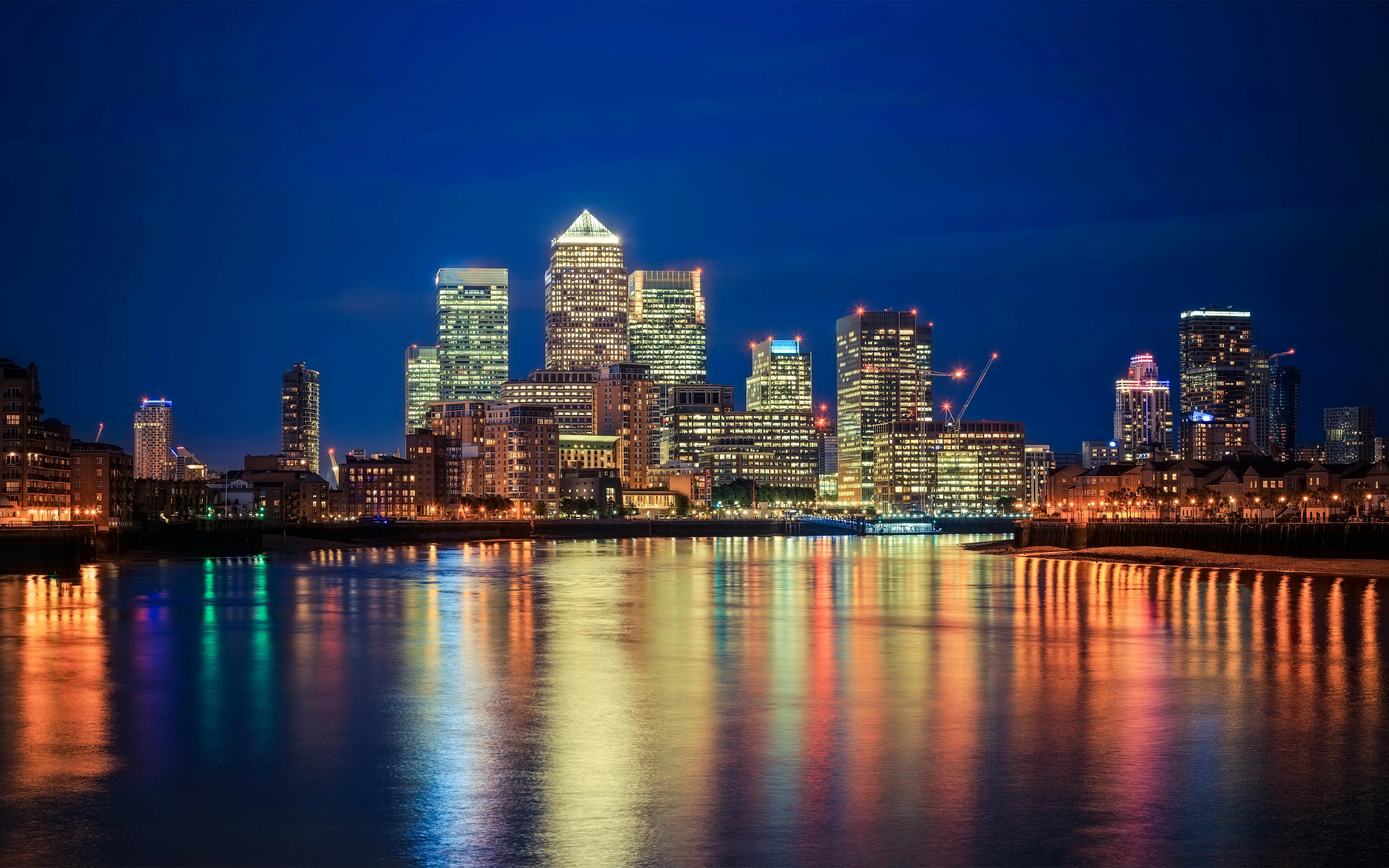 Canary Wharf skyline at night reflecting on Thames River, London.