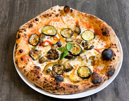 Vegetarian pizza topped with grilled zucchini, eggplant, and peppers on a wooden table.