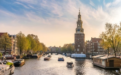 Amsterdam canal with tour boat passing historic buildings and Montelbaanstoren tower.