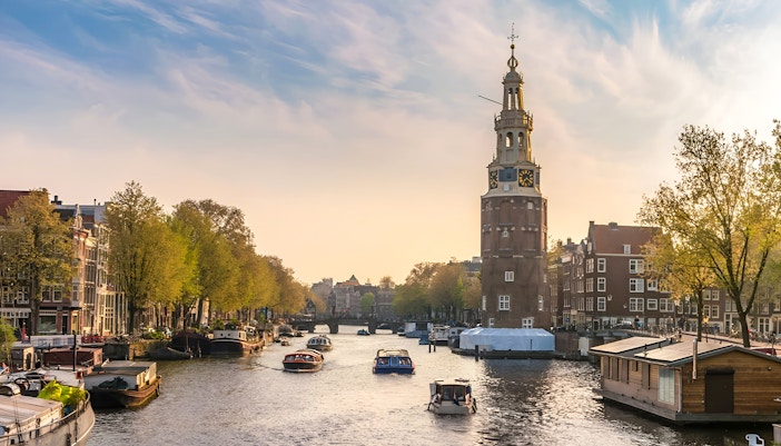 Tour boat on Amsterdam canal passing historic buildings and Montelbaanstoren tower.
