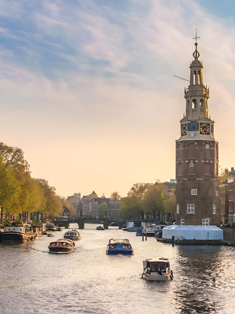 Amsterdam canal with tour boat passing historic buildings and Montelbaanstoren tower.