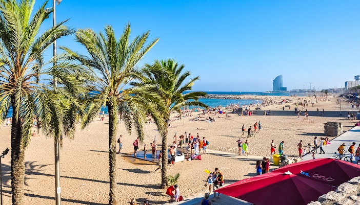 Tourists enjoying a sunny day at Barceloneta Beach, Barcelona, with the Hola Barcelona Travel Card Pass for 2 to 5 days