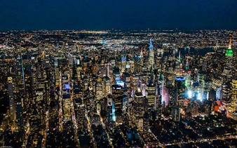 Aerial view of New York City skyline at night, featuring illuminated skyscrapers.