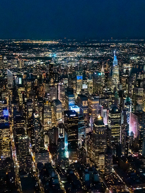 Aerial view of New York City skyline at night, featuring illuminated skyscrapers.