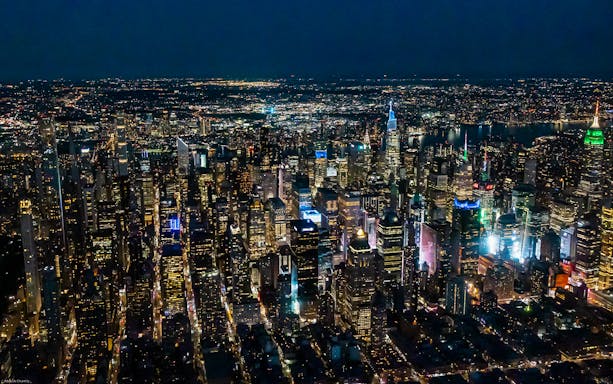 Aerial view of New York City skyline at night, featuring illuminated skyscrapers.