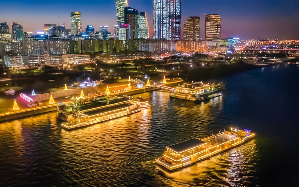 Han River night cruise with illuminated boats and Seoul skyline in the background.