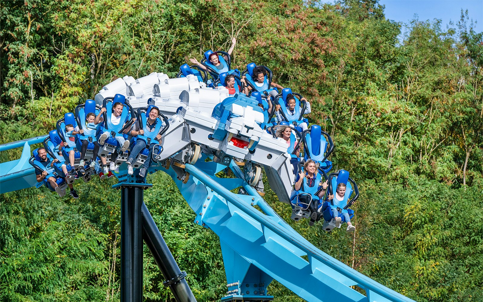 Riders on Maximus Rollercoaster at LegoLand Germany amidst lush greenery.