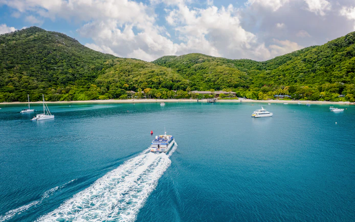 Boat approaching Fitzroy Island with lush hills and clear blue water.