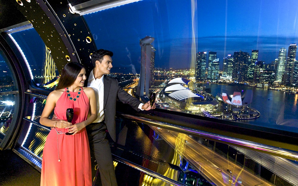 Couple enjoying drinks on Singapore Flyer with city skyline view during New Year's Eve countdown.