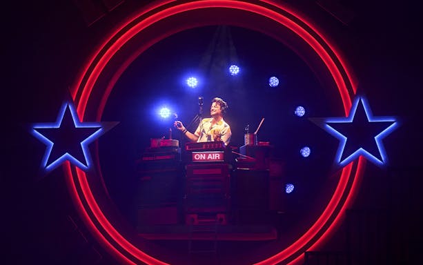 Radio DJ performing on stage with neon stars, Grease musical.