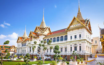 Grand Palace in Bangkok with ornate architecture and manicured gardens.