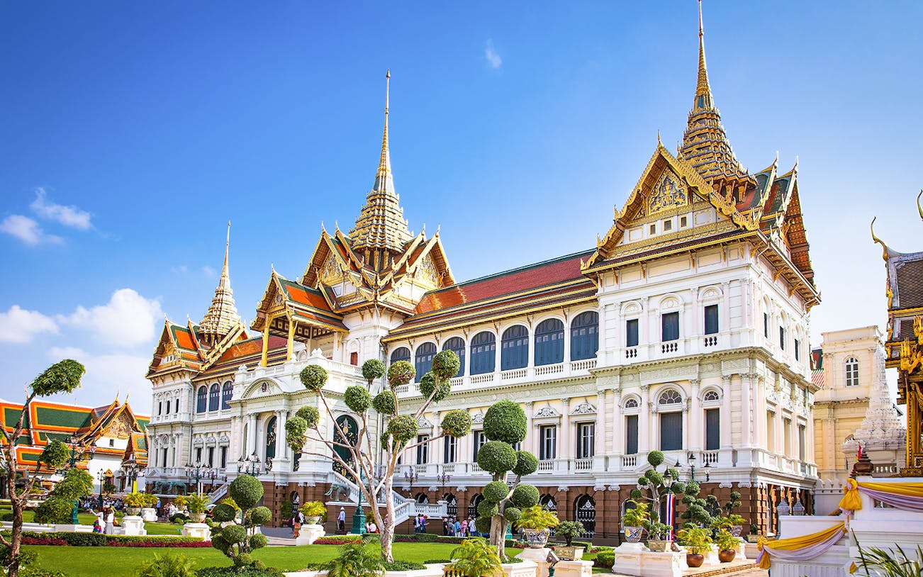 Grand Palace in Bangkok with ornate architecture and manicured gardens.