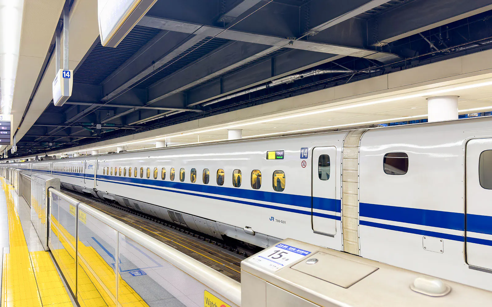 Shinkansen bullet train at station platform in Japan with glass safety barriers and yellow tactile paving.