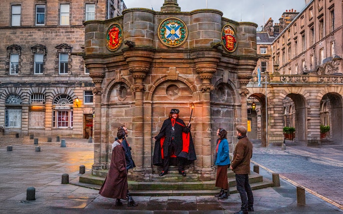 Guide with guests on Ghostly Underground tour in Edinburgh near historic monument.