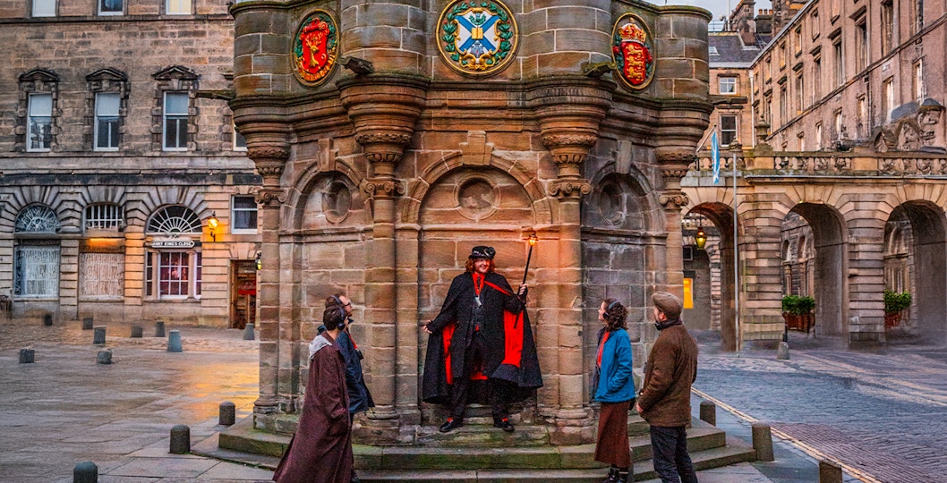 Guide with guests on Ghostly Underground tour in Edinburgh near historic monument.