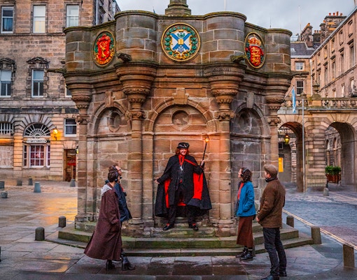 Guide with guests on Ghostly Underground tour in Edinburgh near historic monument.