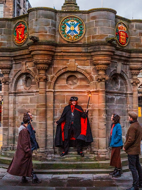 Guide with guests on Ghostly Underground tour in Edinburgh near historic monument.