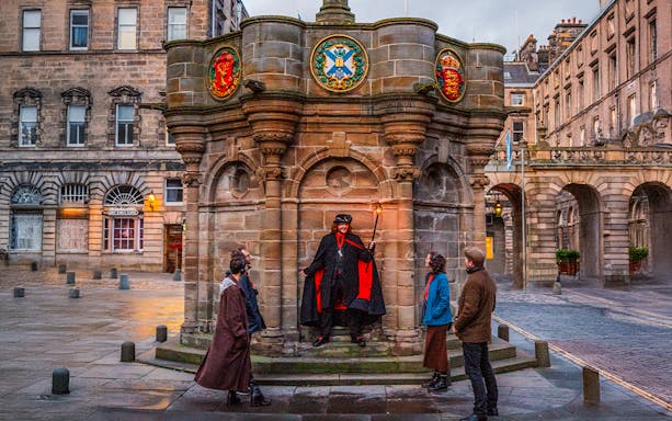 Guide with guests on Ghostly Underground tour in Edinburgh near historic monument.