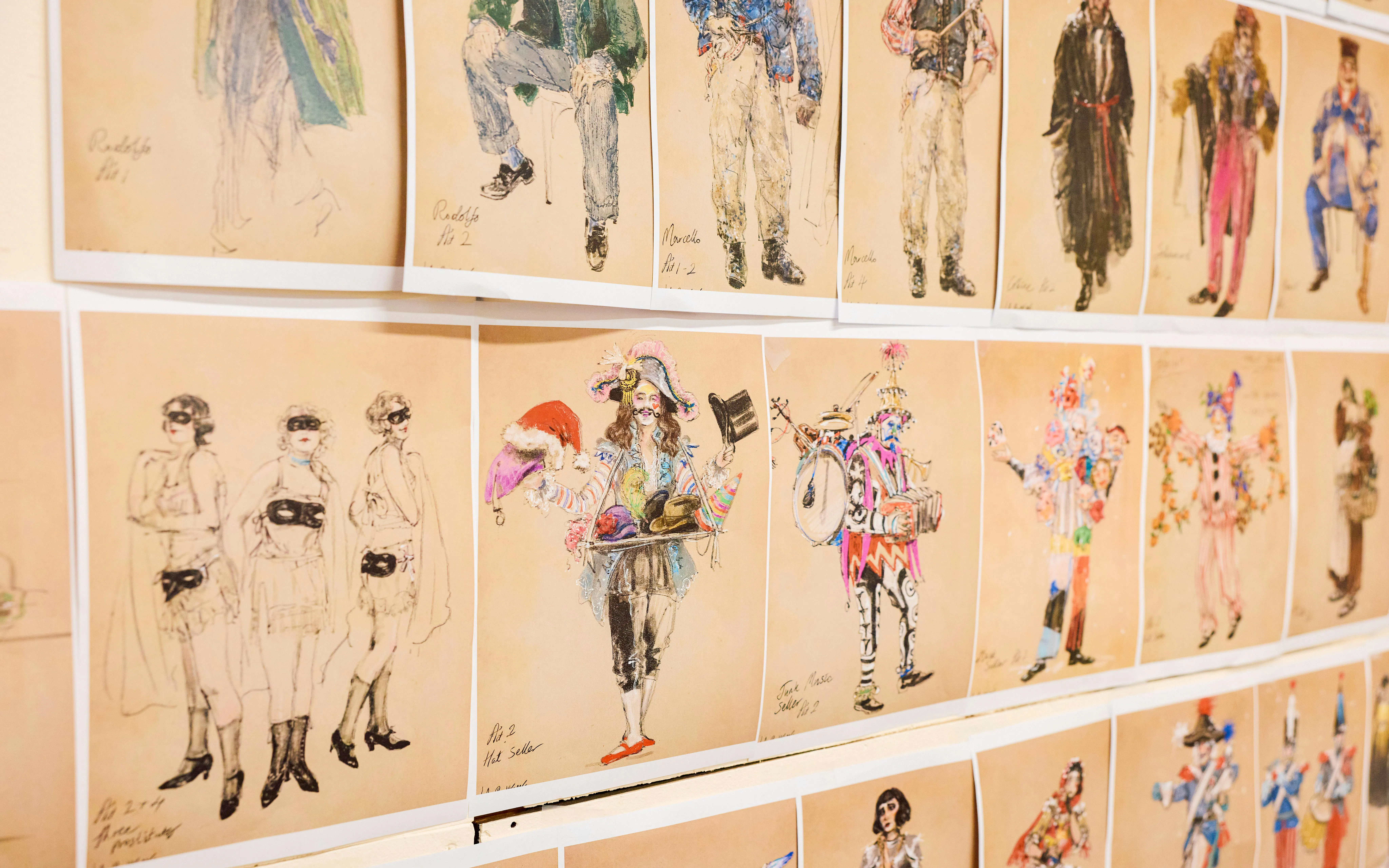 Costume sketches for La Boheme opera characters displayed on a wall.