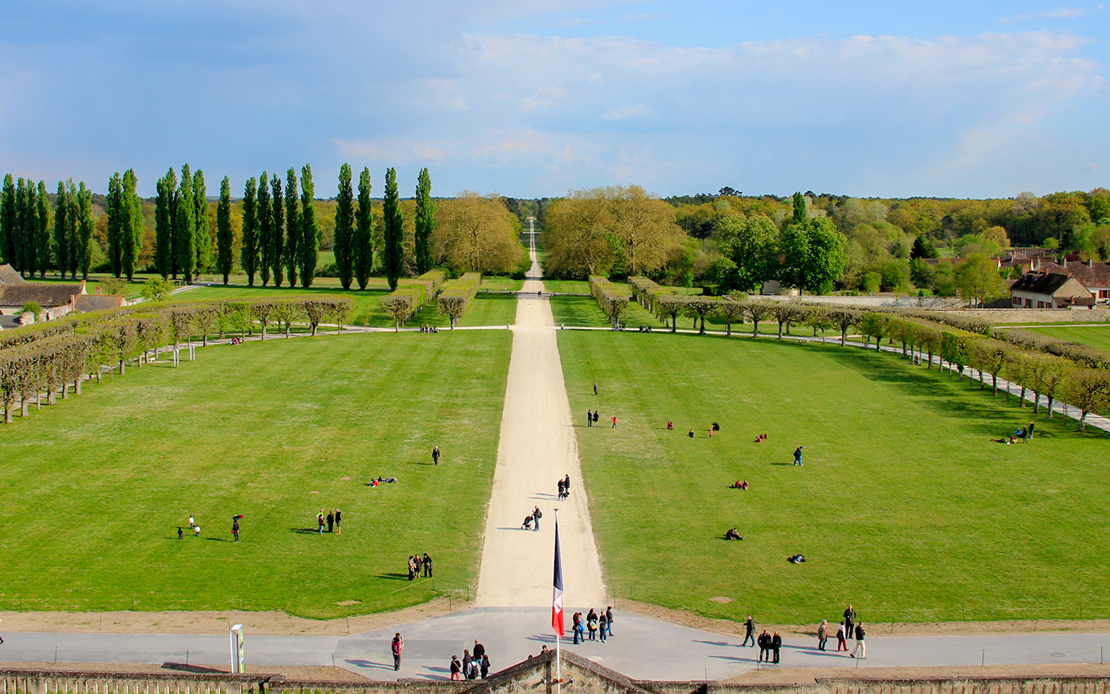 Chambord Castle Gardens with tree-lined paths and visitors enjoying the expansive green lawns.