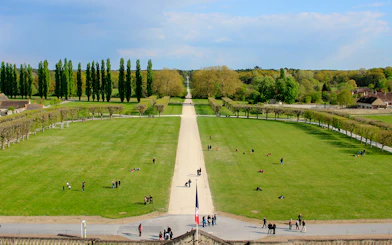 Chambord Castle Gardens with tree-lined paths and visitors enjoying the expansive green lawns.