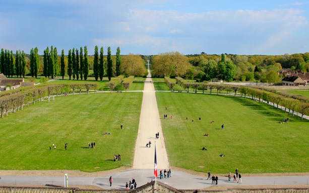 Chambord Castle Gardens with tree-lined paths and visitors enjoying the expansive green lawns.