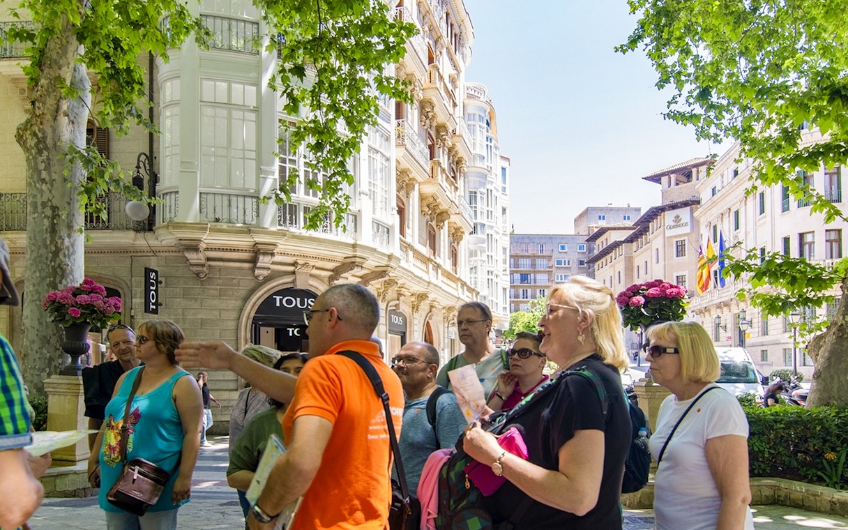 Tourists with guide exploring historic Palma Old Town street.