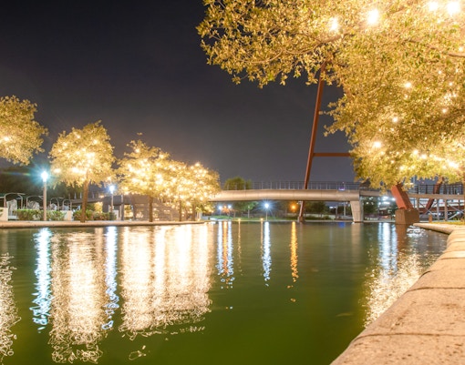 Lights reflecting on canal water at night with illuminated trees and a bridge.