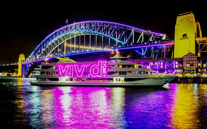 Cruise ship with "Vivid Sydney" lights passing Sydney Harbour Bridge at night.