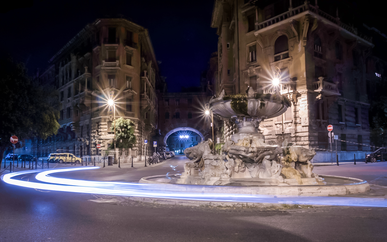 Fountain in Coppedè district, Rome, illuminated at night with light trails from passing cars.