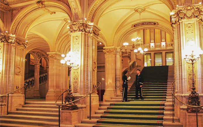 Vienna State Opera grand staircase with ornate arches and staff in formal attire.