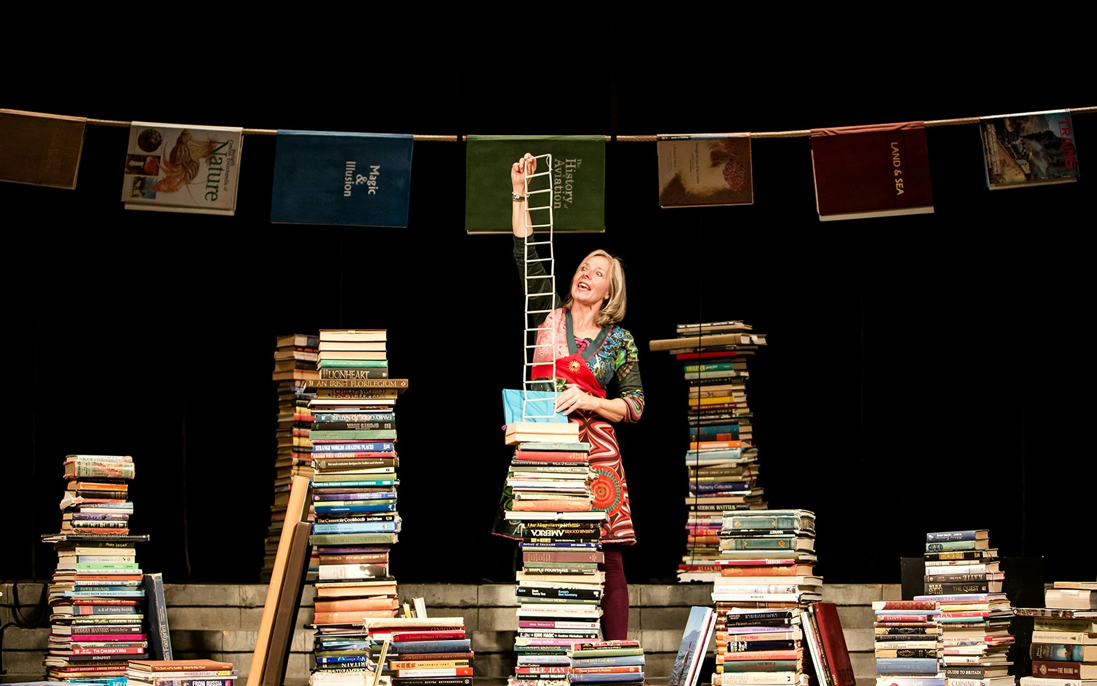 Woman performing among stacks of books on stage, related to "I Believe In Unicorns" tour.
