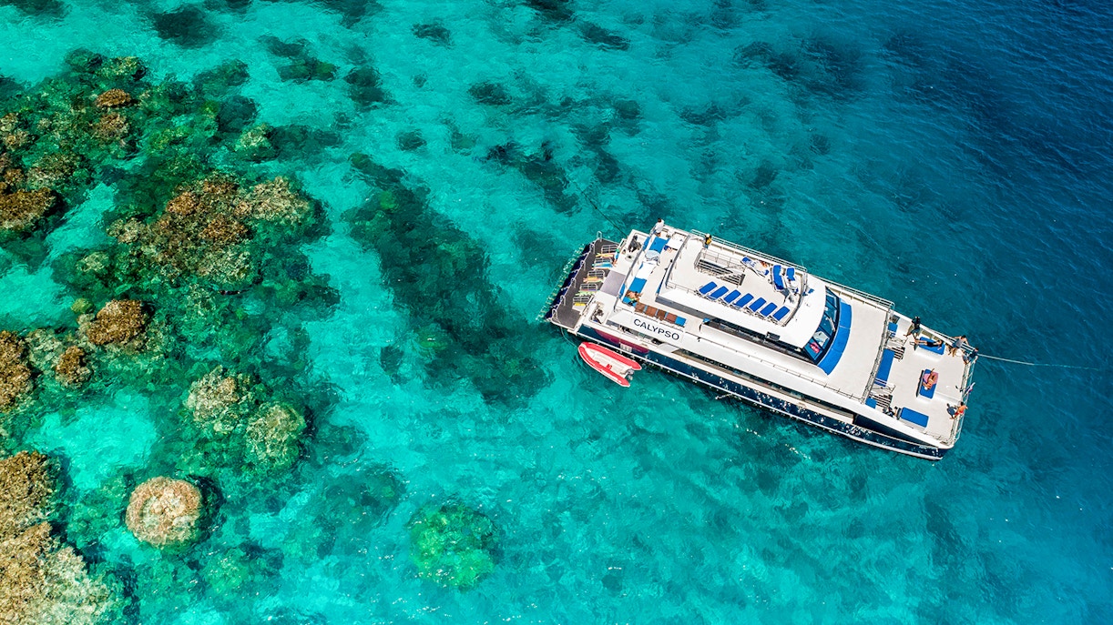 Cruise ship anchored on the Outer Great Barrier Reef with coral formations visible below.