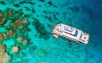 Cruise ship anchored on the Outer Great Barrier Reef with coral formations visible below.