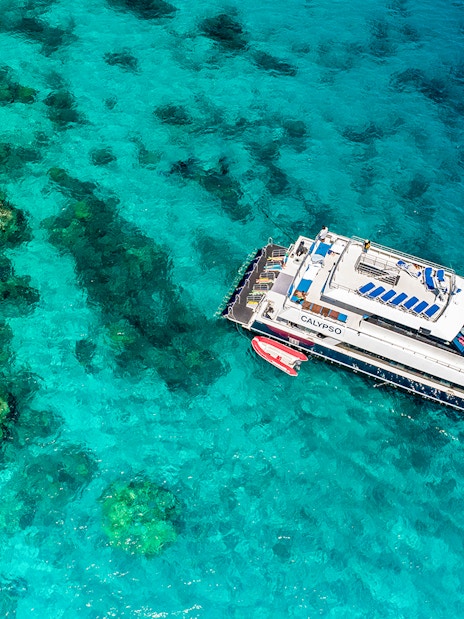 Cruise ship anchored on the Outer Great Barrier Reef with coral formations visible below.