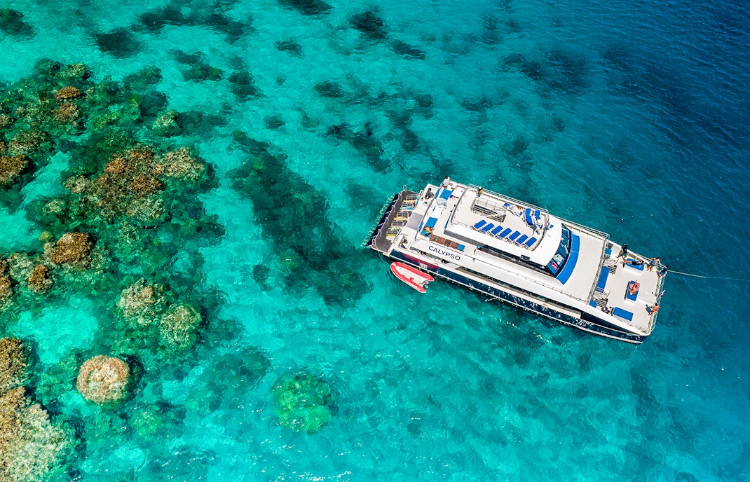 Cruise ship anchored on the Outer Great Barrier Reef with coral formations visible below.