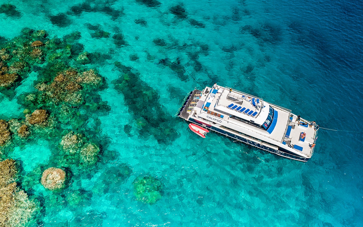 Cruise ship anchored on the Outer Great Barrier Reef with coral formations visible below.