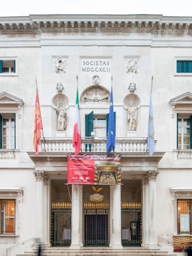 Facade of Teatro La Fenice in Venice with flags and statues.