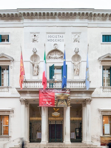 Facade of Teatro La Fenice in Venice with flags and statues.