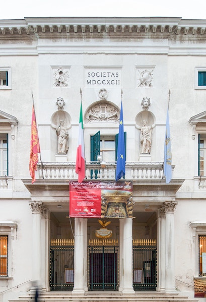 Facade of Teatro La Fenice in Venice with flags and statues.