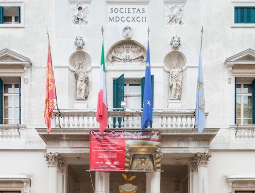 Facade of Teatro La Fenice in Venice with flags and statues.