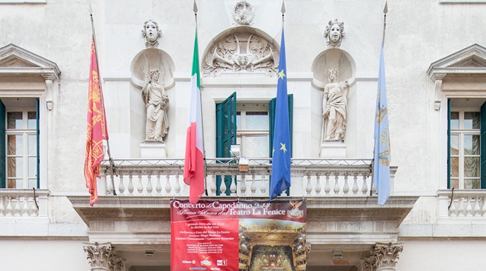 Facade of Teatro La Fenice in Venice with flags and statues.