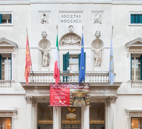Facade of Teatro La Fenice in Venice with flags and statues.