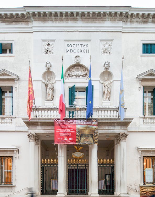 Facade of Teatro La Fenice in Venice with flags and statues.