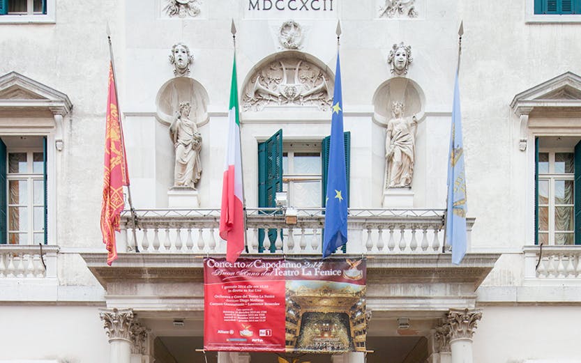 Facade of Teatro La Fenice in Venice with flags and statues.