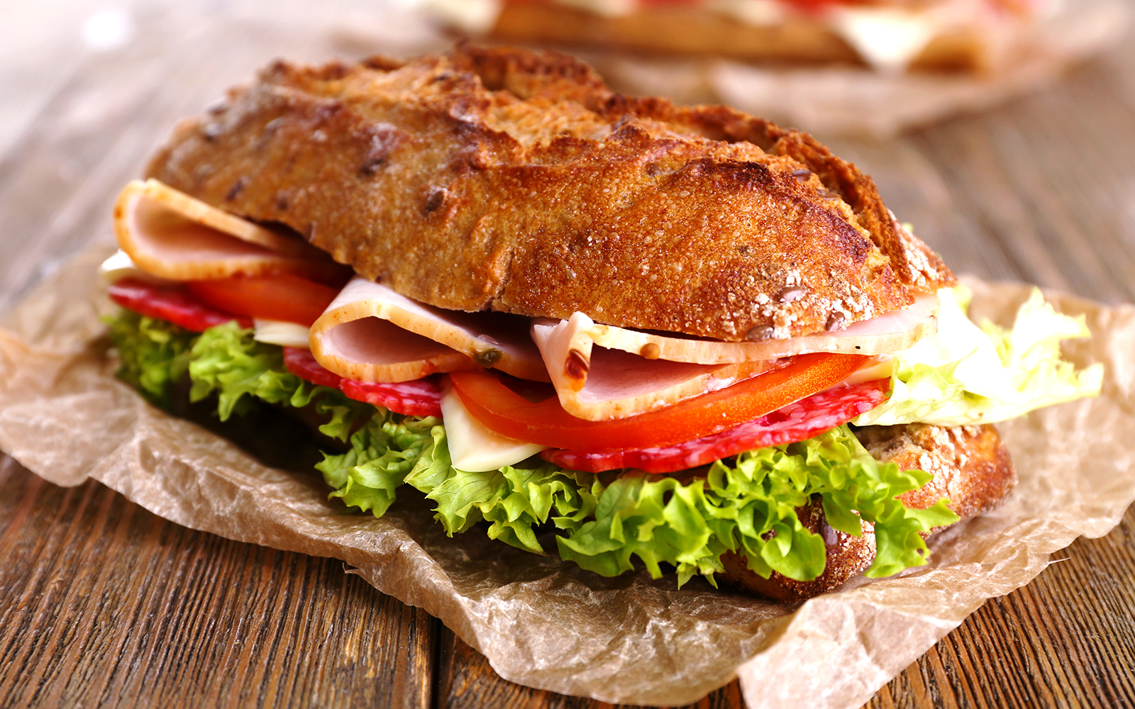 Baguette sandwich with ham, cheese, lettuce, and tomato on a wooden table in Barcelona.
